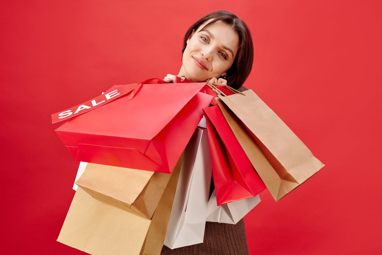 A cheerful woman holding multiple shopping bags with a sale on a red background.